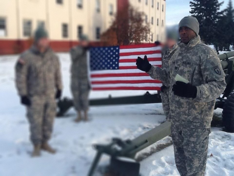 Captain Banks addressing soldiers in front of the American flag in the snow.